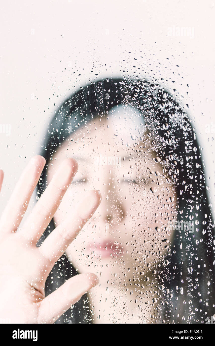 Asian woman with closed eyes behind window pane with water drops Stock Photo Alamy
