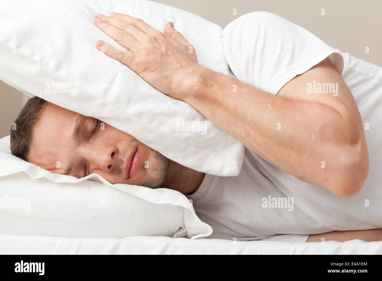 Portrait of Young Caucasian man in bed hiding from noise Stock Photo