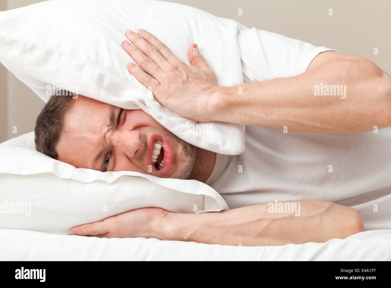 Portrait of Young Caucasian man in bed angry about noise Stock Photo