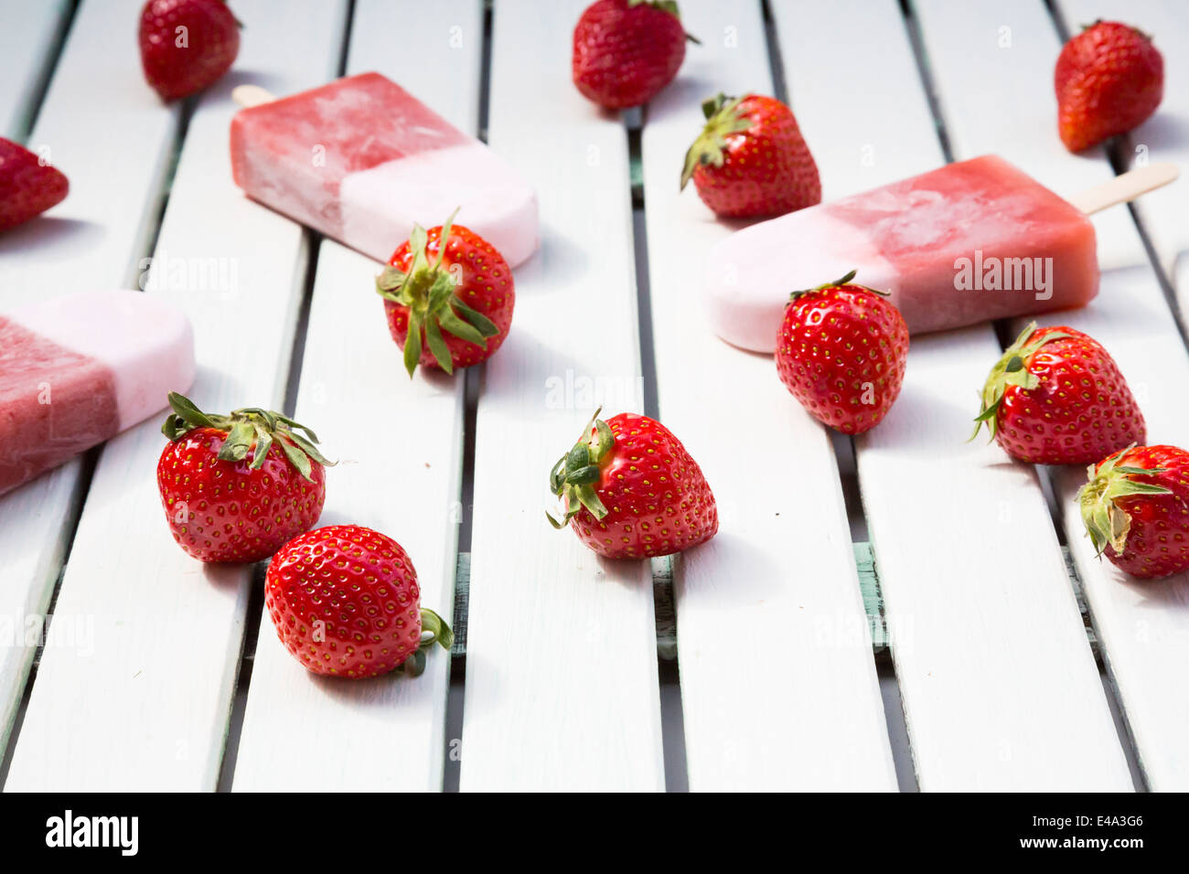Three strawberry ice cream lollies and strawberries on white wood Stock