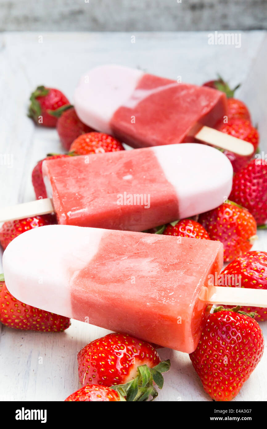 Three strawberry ice cream lollies and strawberries on white wood Stock