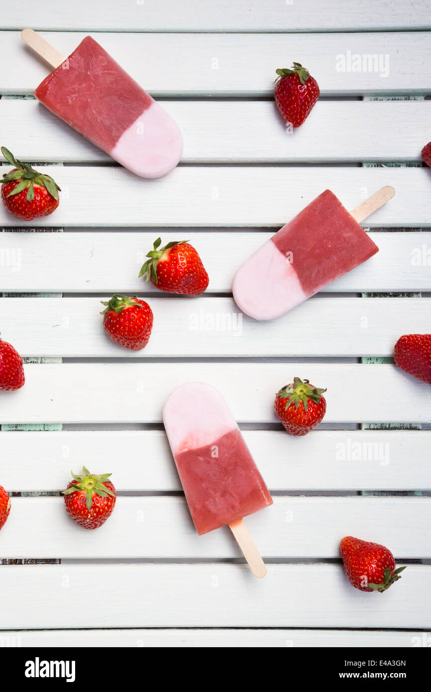 Three strawberry ice cream lollies and strawberries on white wood Stock
