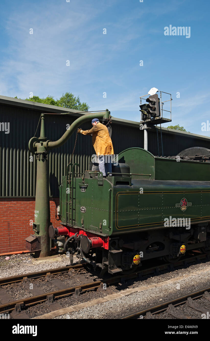 Man filling up steam engine train with water in summer