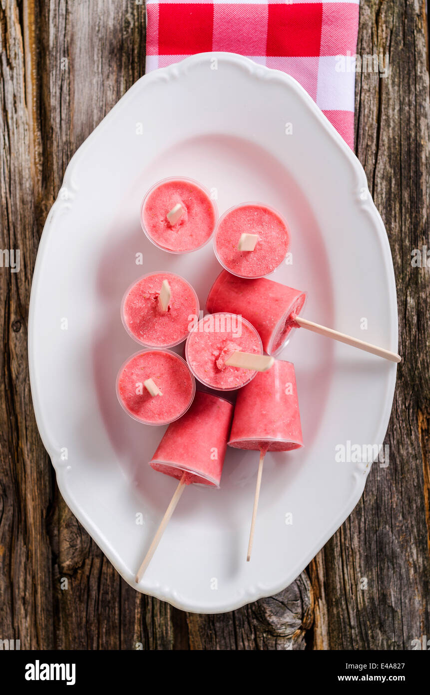 Plate of home-made strawberry ice lollies on wood, elevated view Stock Photo