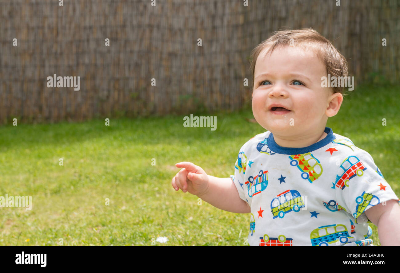 A little boy pointing and smiling in the garden during summer Stock Photo