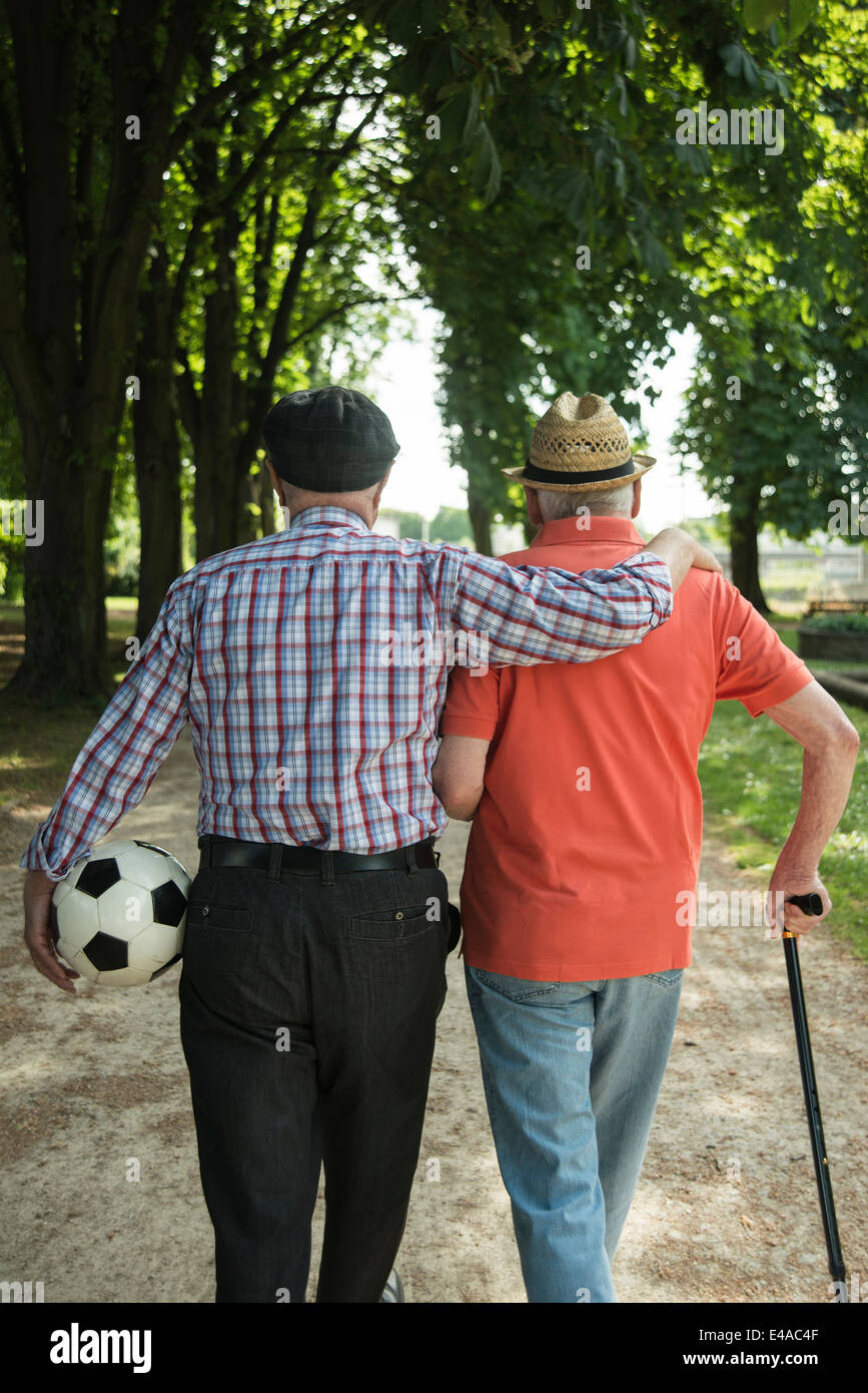Two old friends walking in the park with football, back view Stock Photo