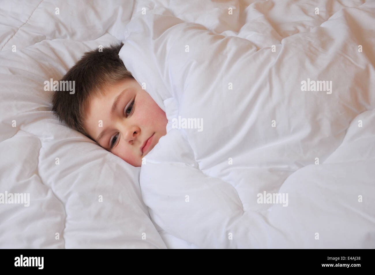 sick  boy schoolboy seven years old lies bed laid blanket white grieves sad thoughtful one Stock Photo