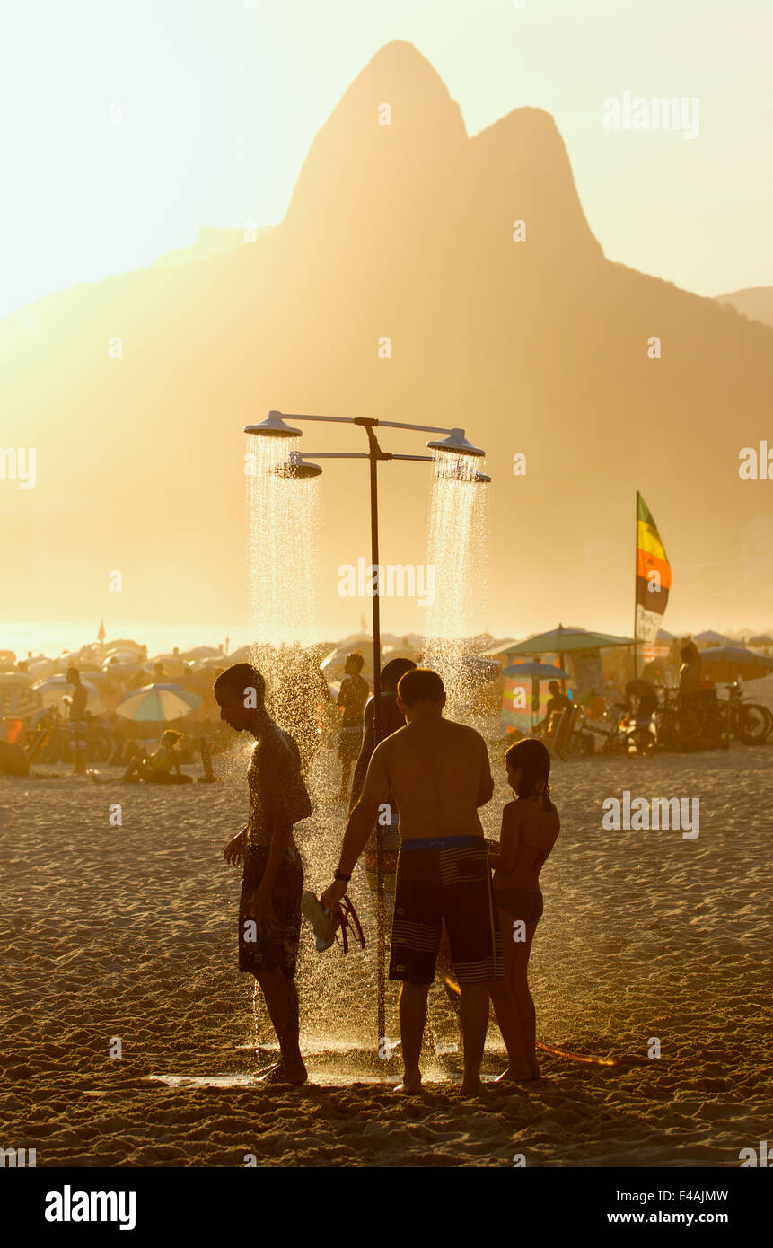 RIO DE JANEIRO, BRAZIL - JANUARY 25, 2014: Group of Brazilians stand under the outdoor showers on Ipanema Beach at sunset. Stock Photo