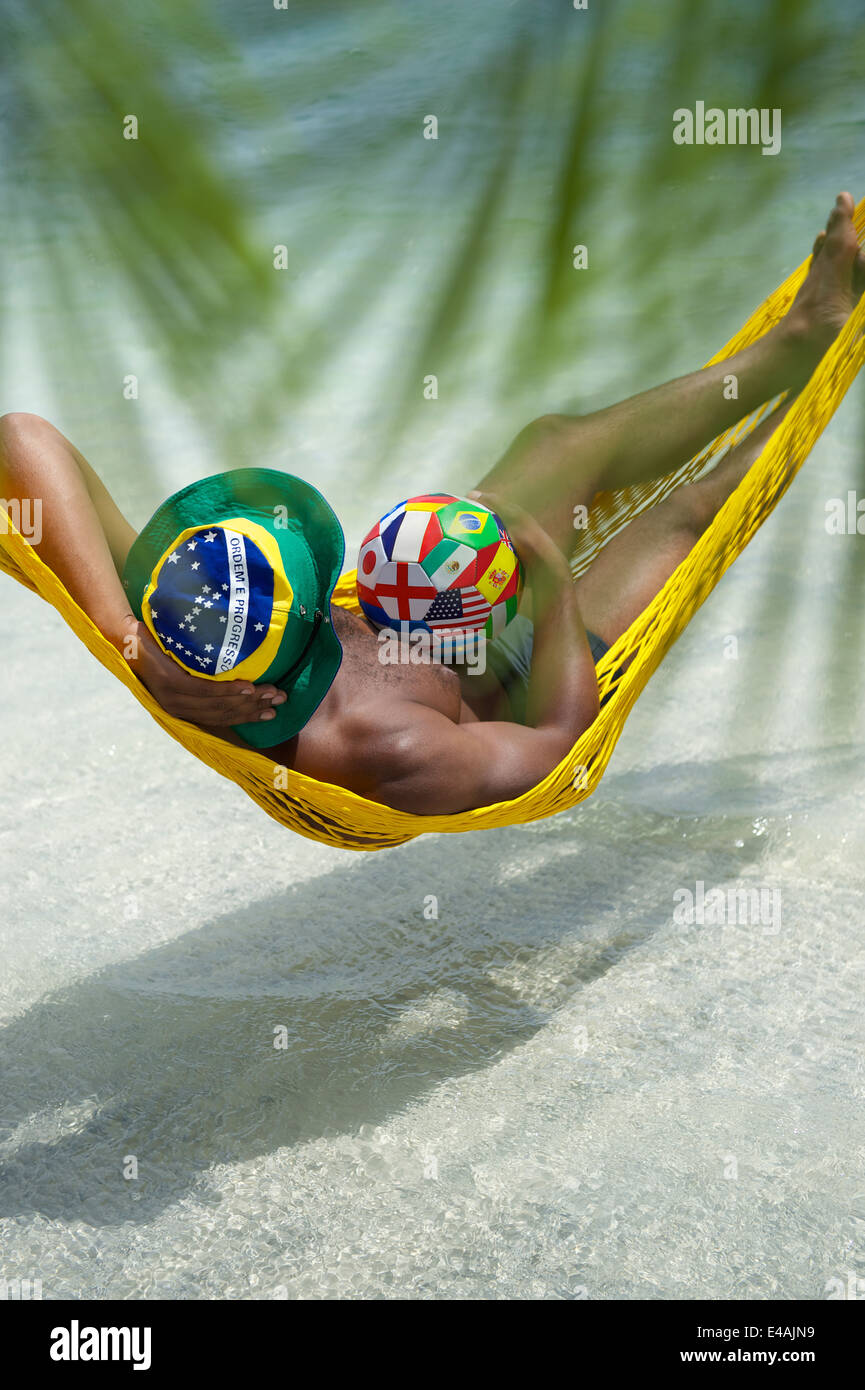 Brazilian football player relaxing in beach hammock with international team flag soccer ball Stock Photo