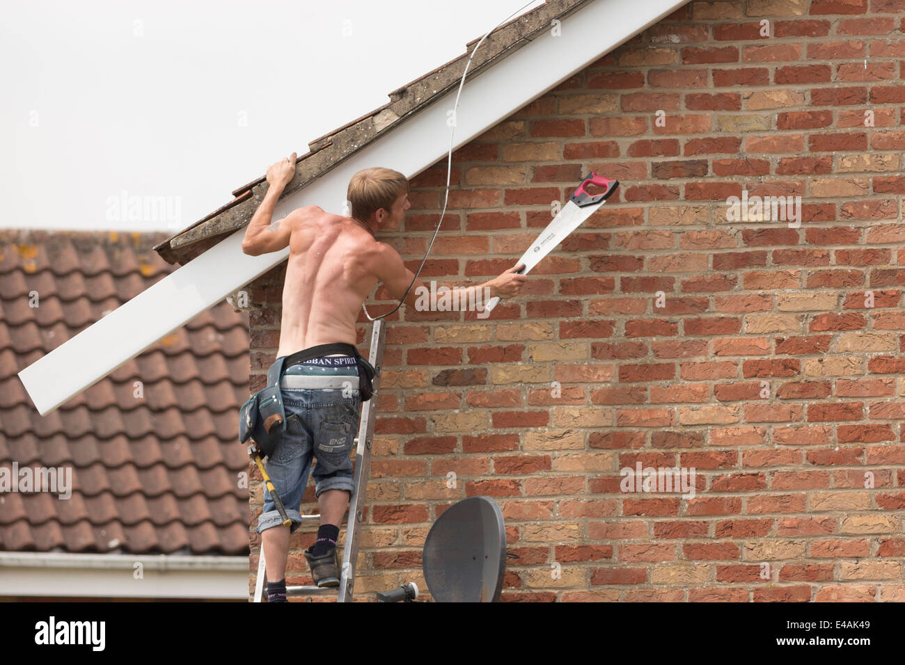 Workman replacing fascia boards on a house roof. Stock Photo