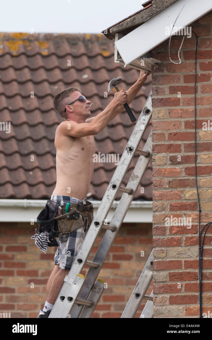 Workman replacing fascia boards on a house roof. Stock Photo
