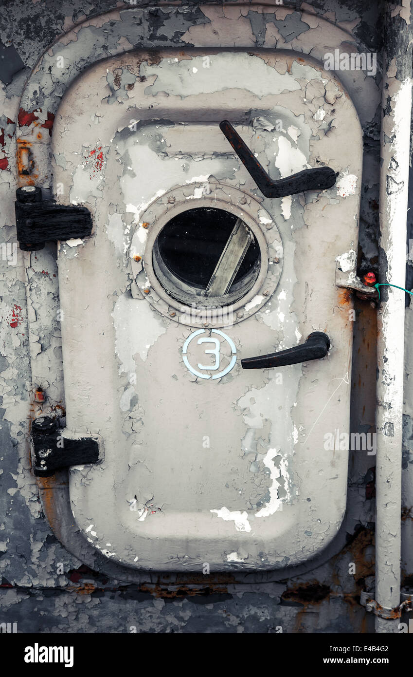 Old gray ship door with porthole and handles Stock Photo