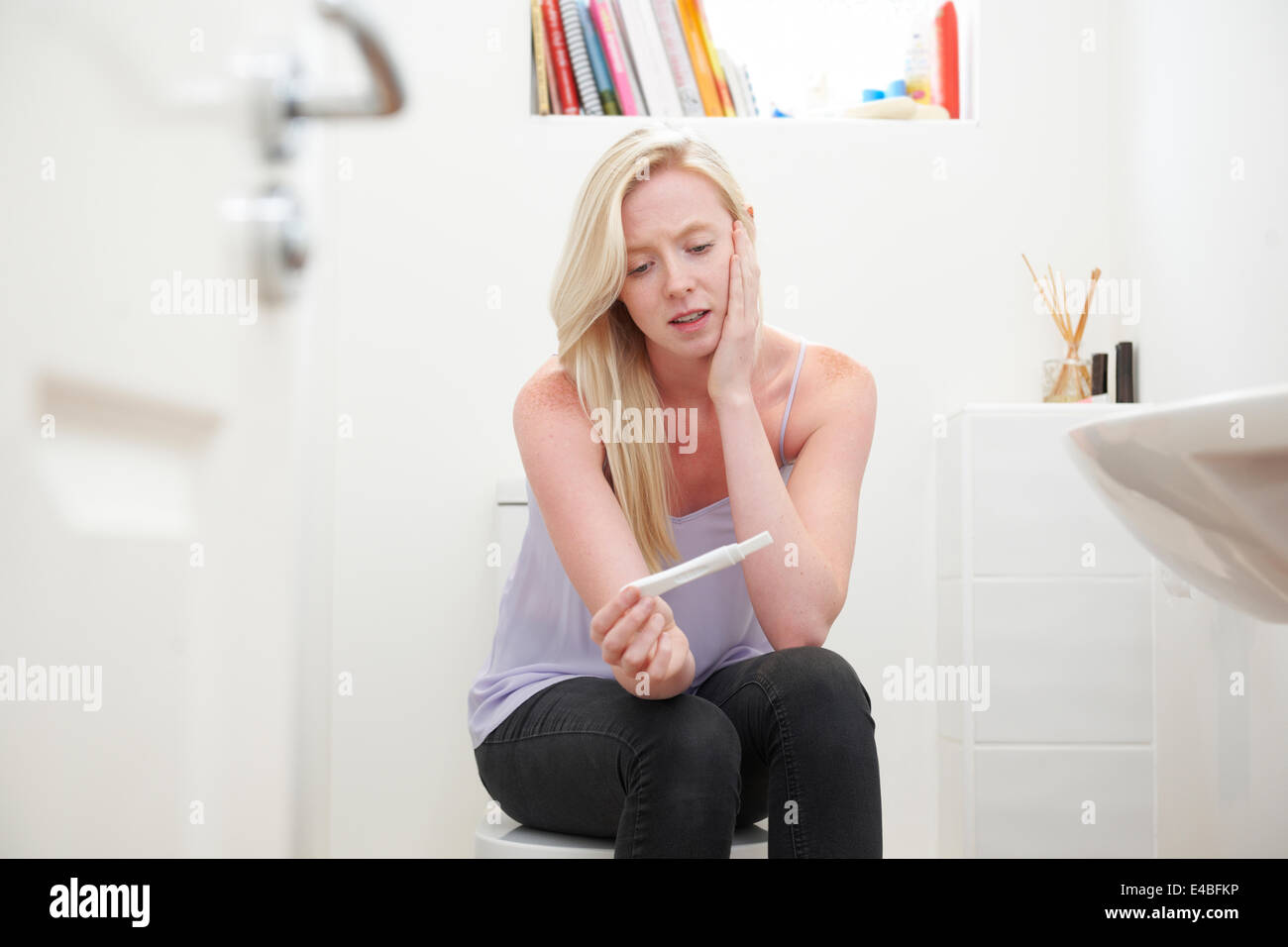 Worried Teenage Girl Sitting In Bathroom With Pregnancy Test Stock Photo