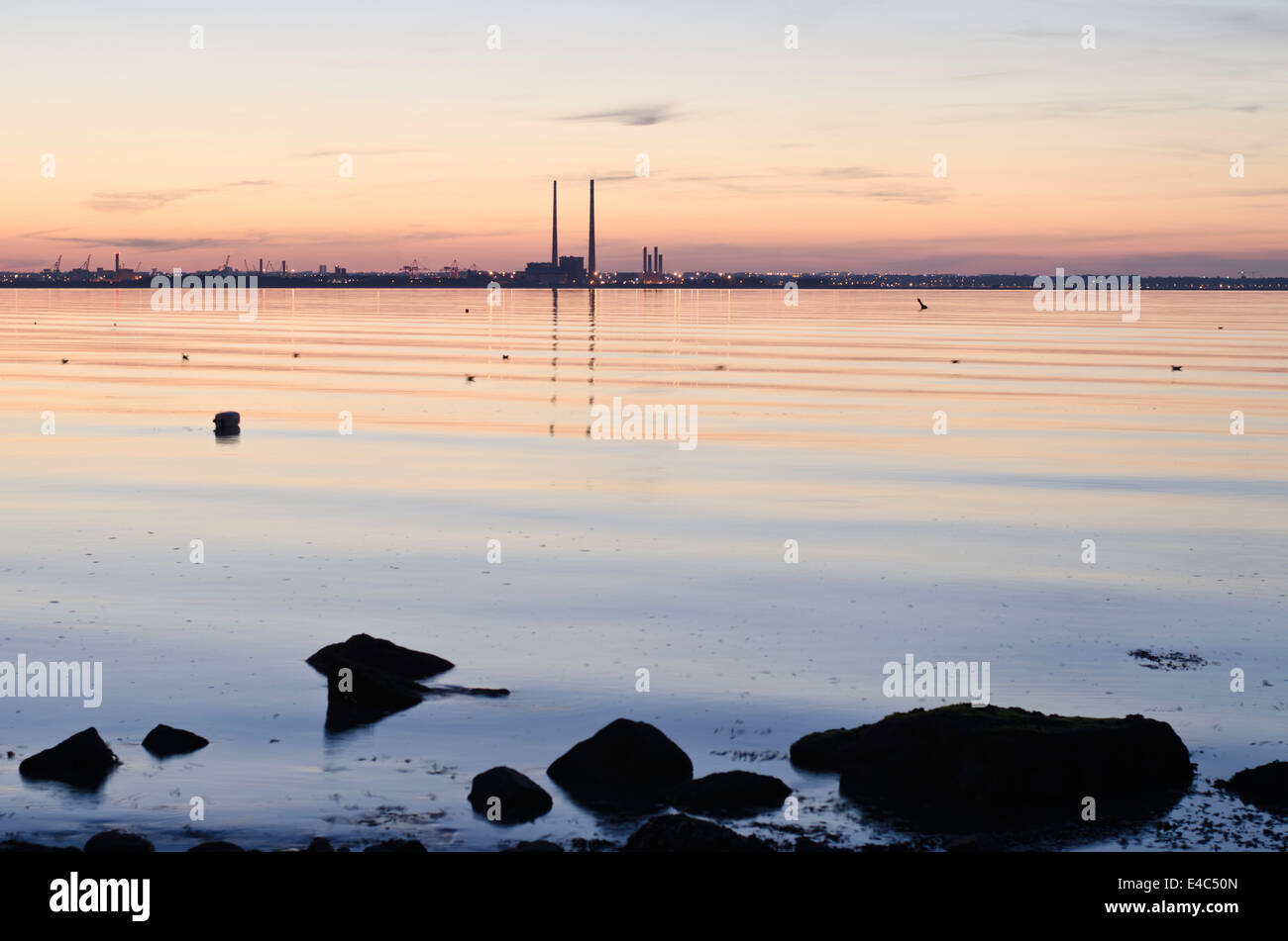 Calm sea with ripples at dusk and chimneys of power plant on horizon. Stock Photo