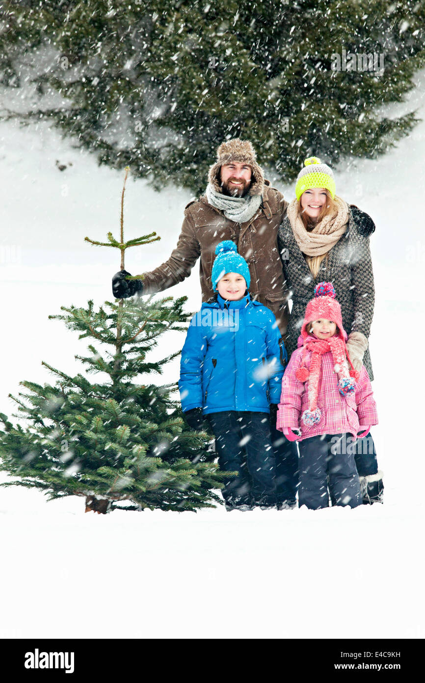 Family with two children stands with Christmas tree in snow-covered landscape, Bavaria, Germany Stock Photo