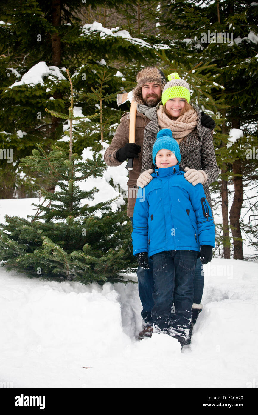Parents and son standing with axe by Christmas tree in snow-covered landscape, Bavaria, Germany Stock Photo
