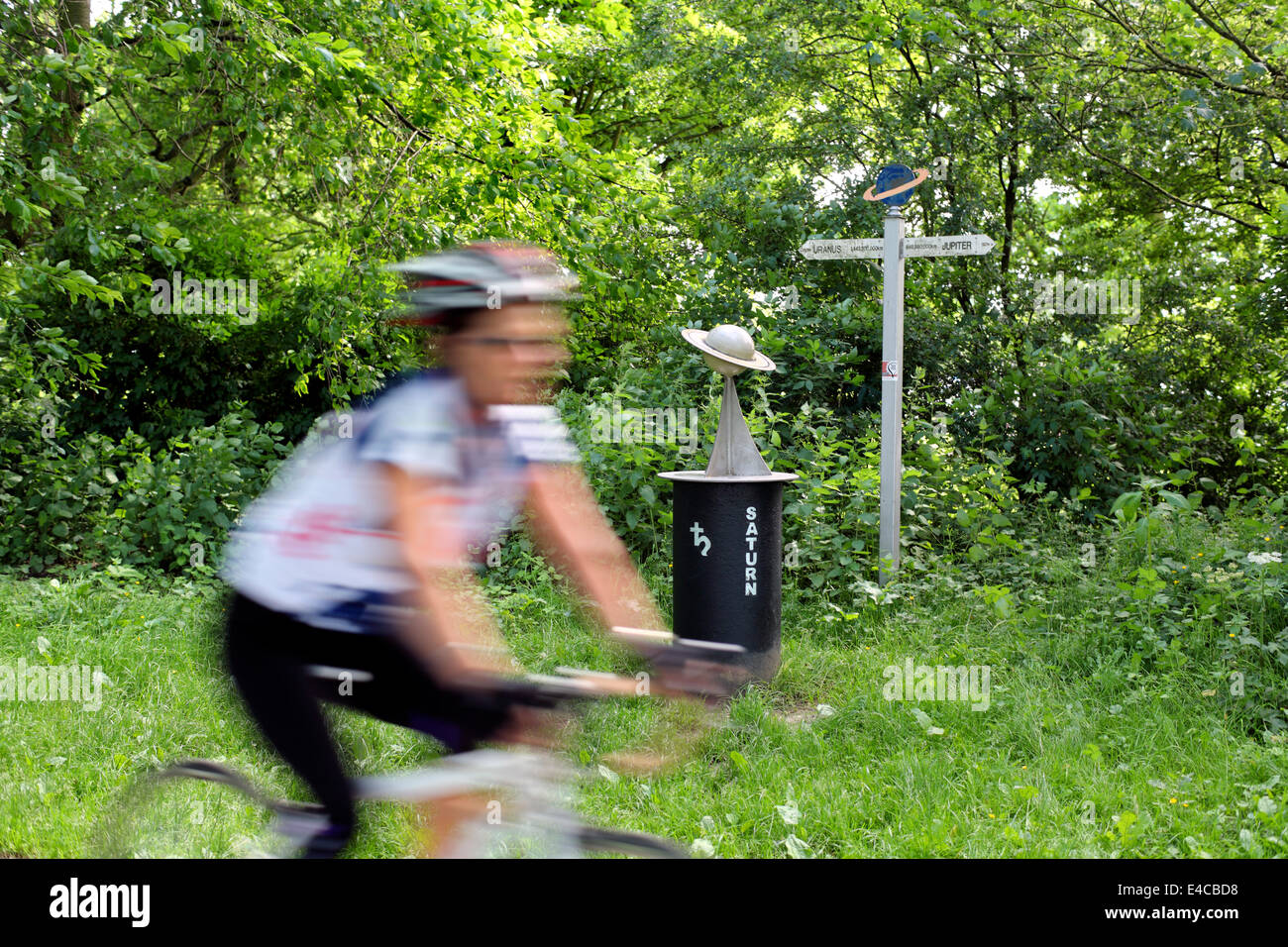 A cyclist passes a model of the planet Saturn on the York to Selby solar cycle path. Stock Photo