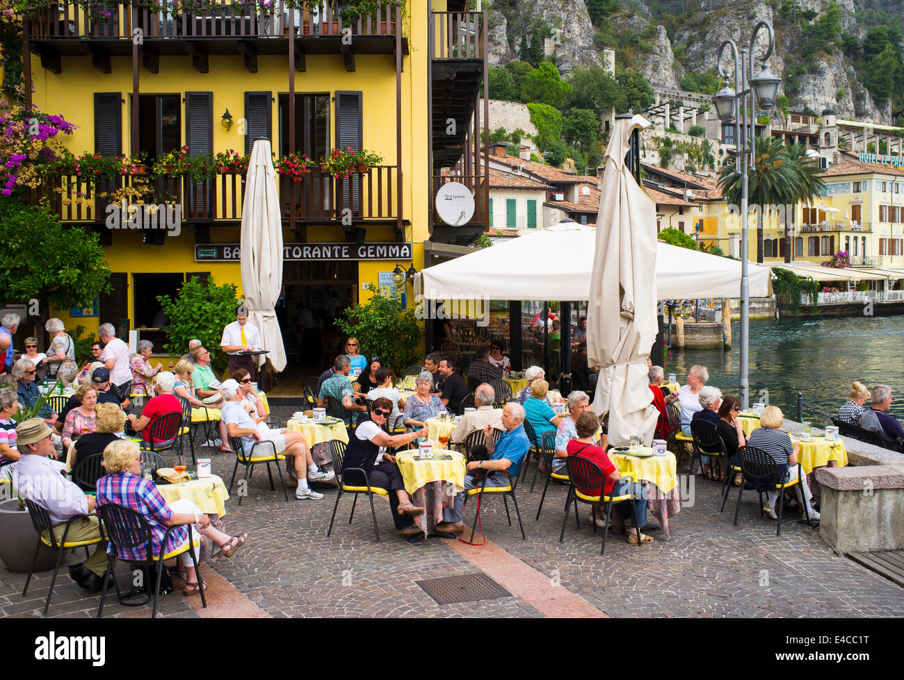 Holidaymakers dining al fresco outside a restaurant in the picturesque resort of Limone on the banks of Lake Garda, Italy. Stock Photo