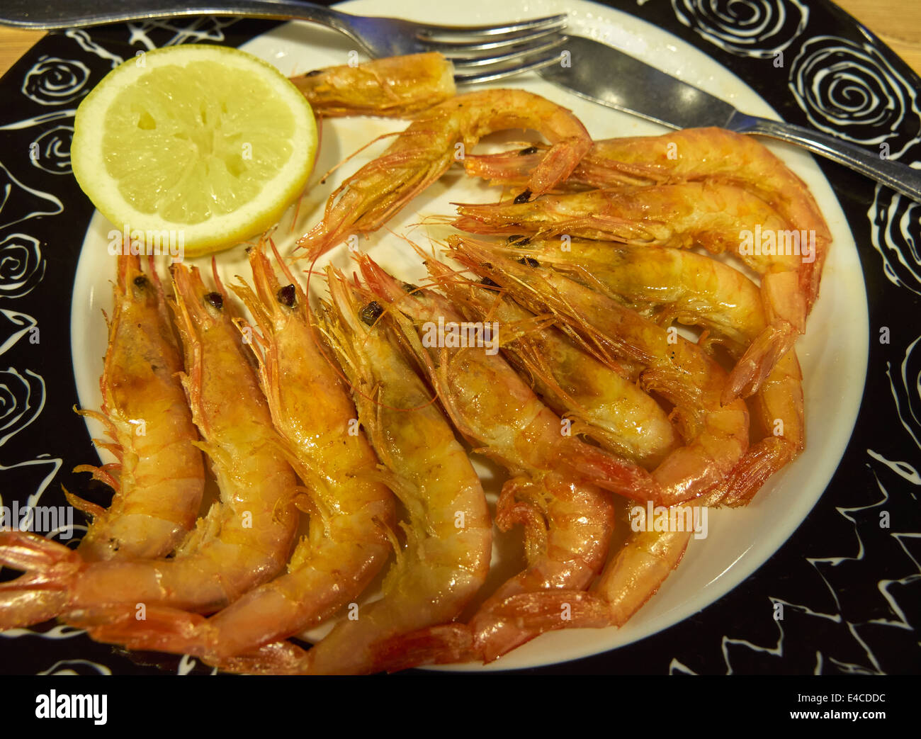 A dish of sauteed scampi. Whole shell on prawns are sauteed in butter, garlic, and white wine and served with half a lemon. Stock Photo