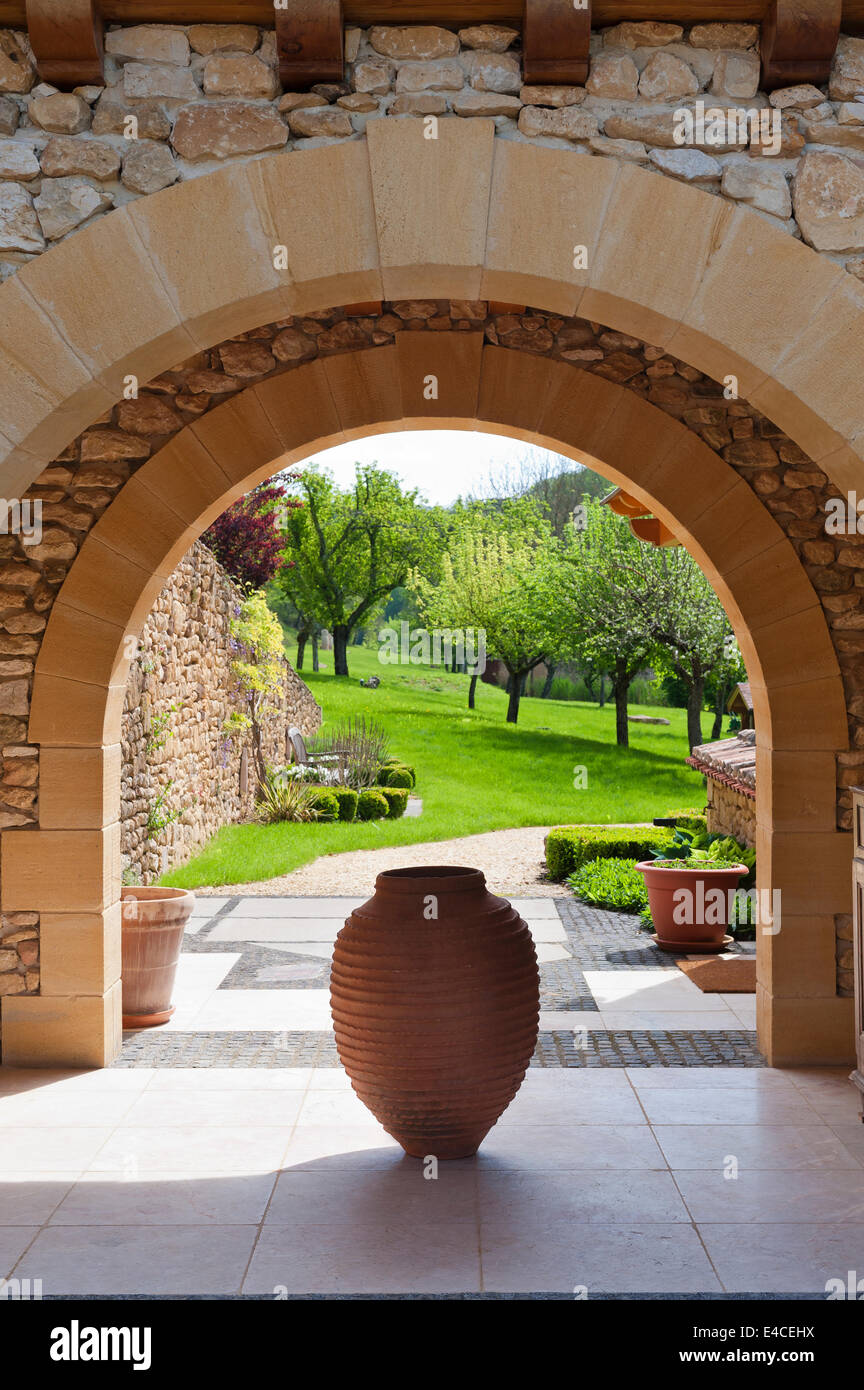 An antique Spanish terracotta 'tinaja' jar stands within an arched loggia looking out to garden Stock Photo