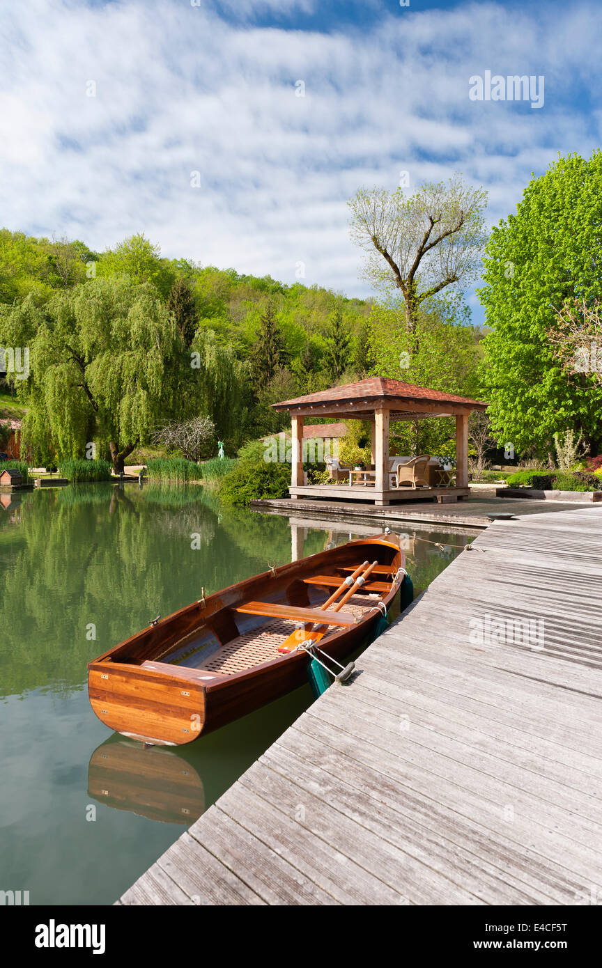 A lakeside pavilion with wooden rowing boat moored by deck Stock Photo