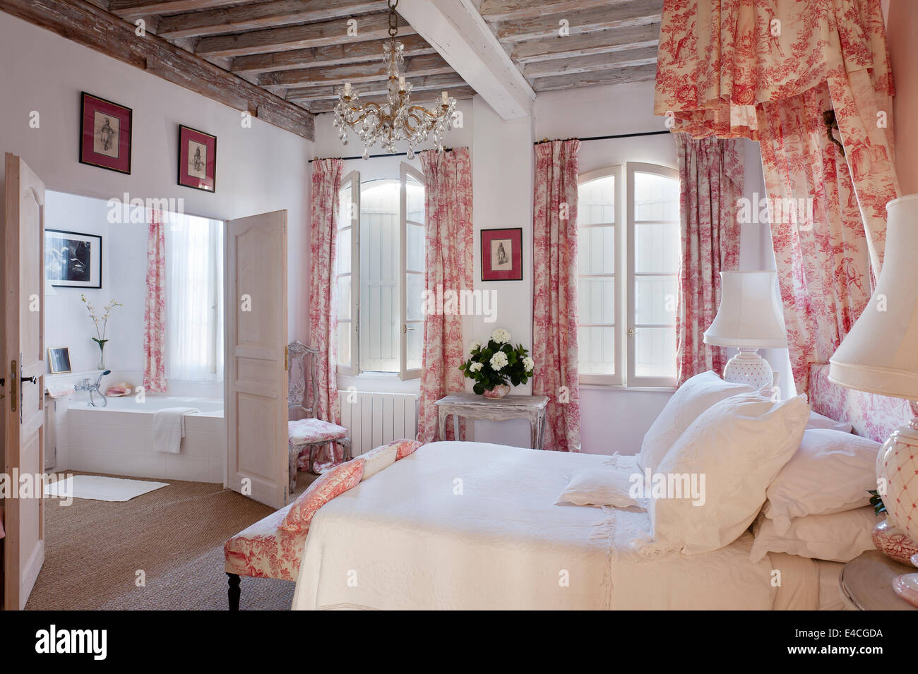 Pink and white toile de jouy fabric on cushions, curtain and bed coronet canopy in bedroom with wooden ceiling beams and bedside Stock Photo