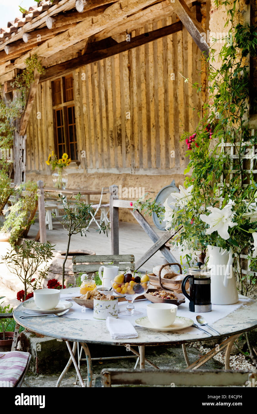 Breakfast laid on round table with folding bistro chairs in courtyard by old barn Stock Photo