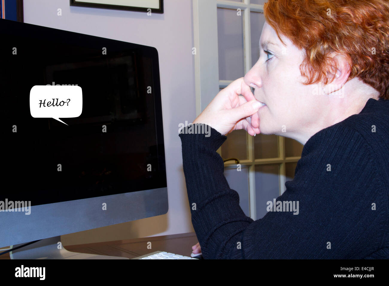 Mature woman at a home office computer looking with trepidation at a conversation bubble with the work Hello. Stock Photo