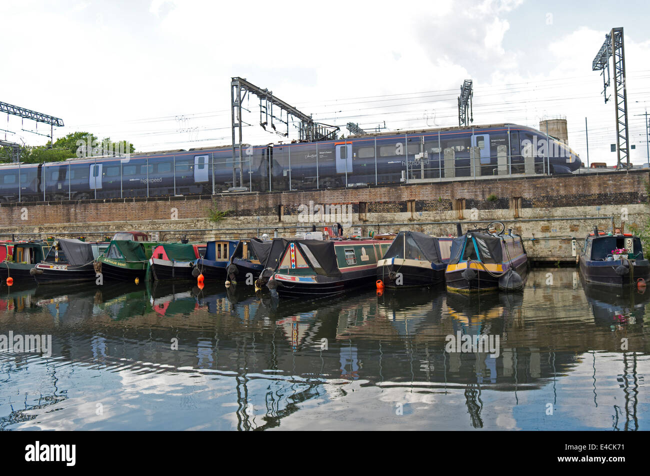 A Eurostar train passes alongside canal boats moored in the Regent's Canal in King's Cross, London. Stock Photo