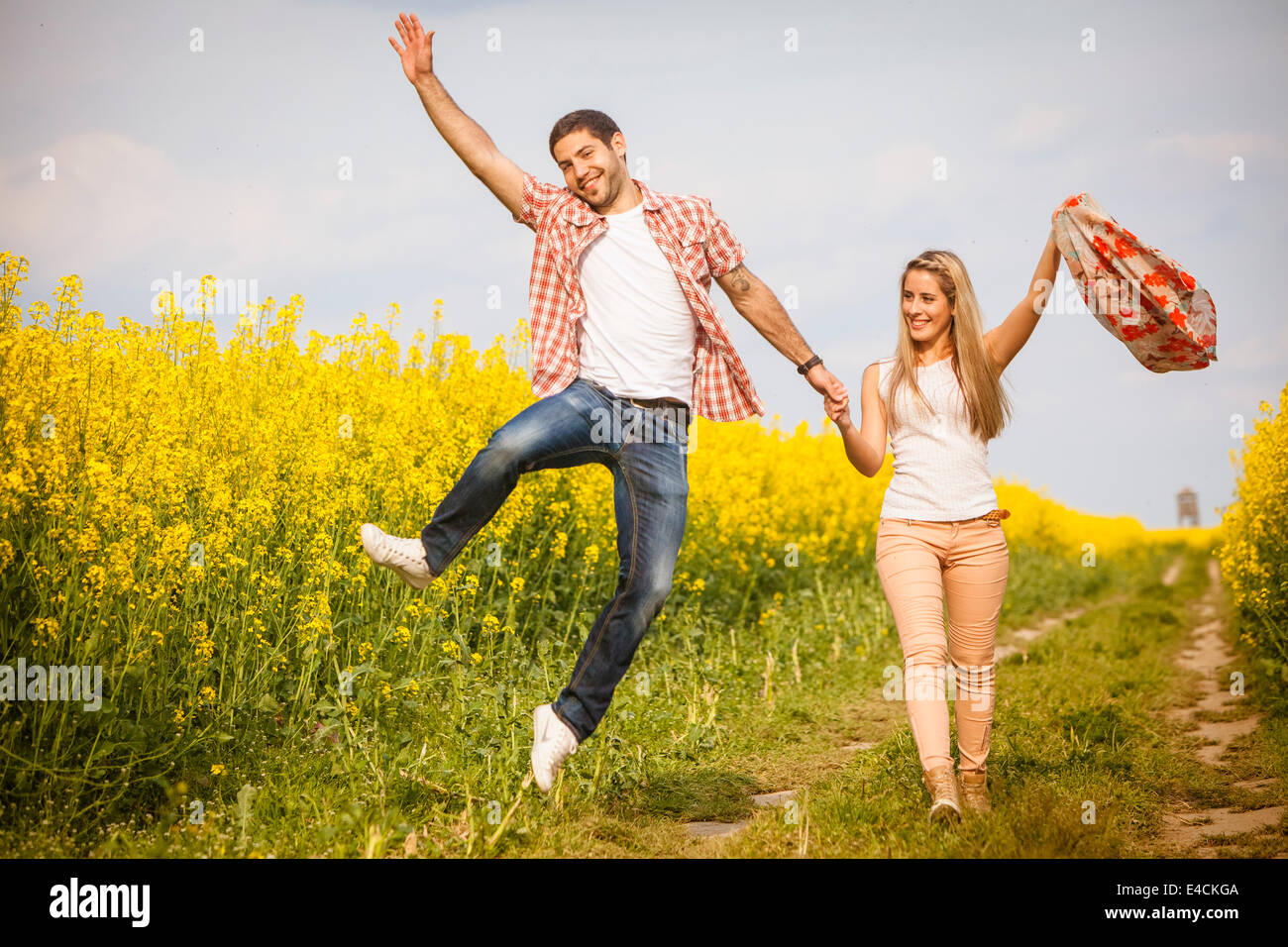 Happy young couple holding hands by colza field, Tuscany, Italy Stock Photo