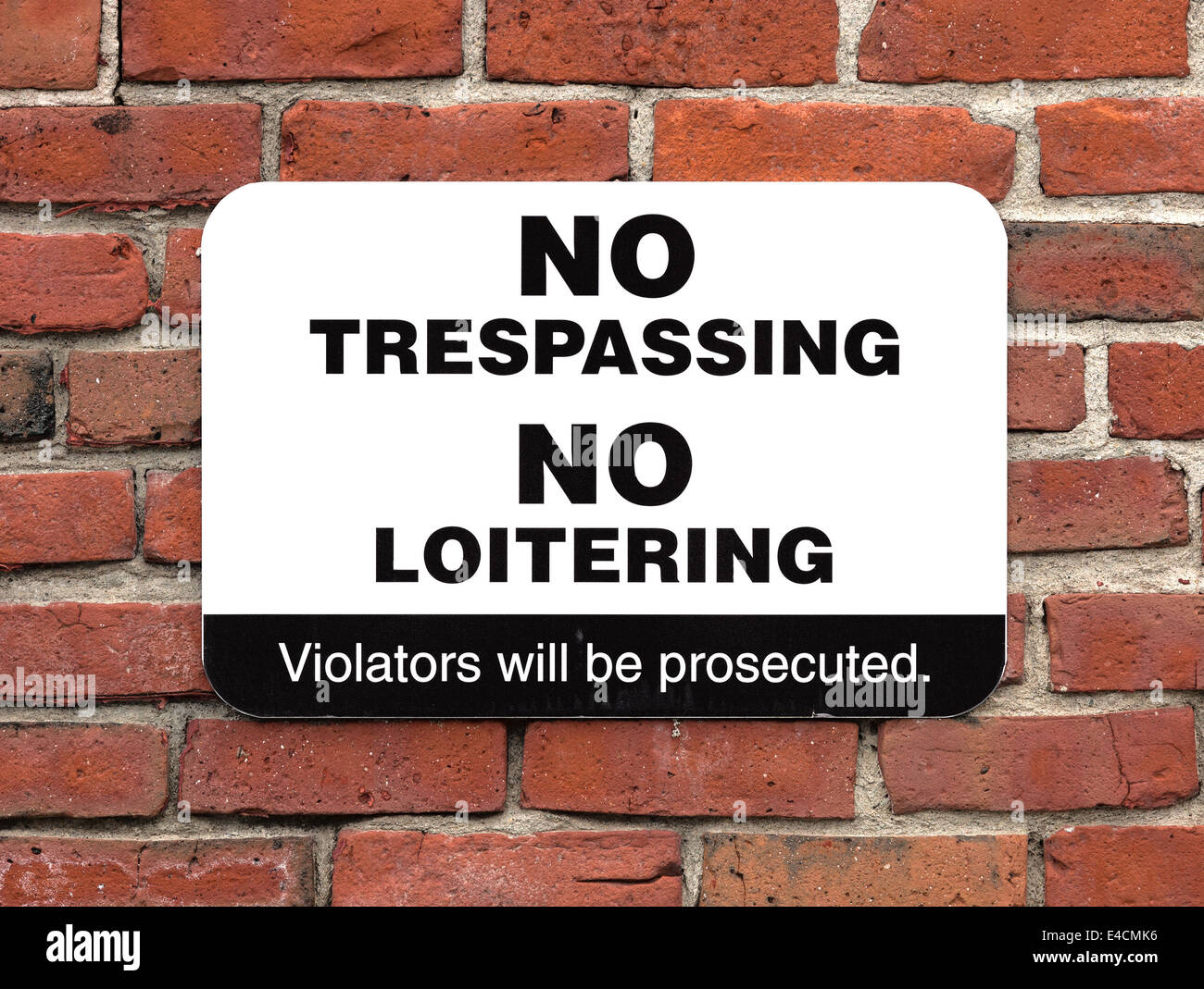 A bold no trespassing no loitering sign attached to an old brick wall. Stock Photo