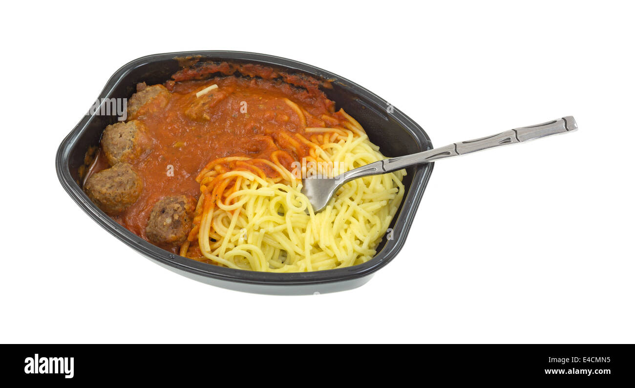 A microwaved spaghetti and meatball TV dinner in a black tray with a fork inserted into the pasta on a white background. Stock Photo