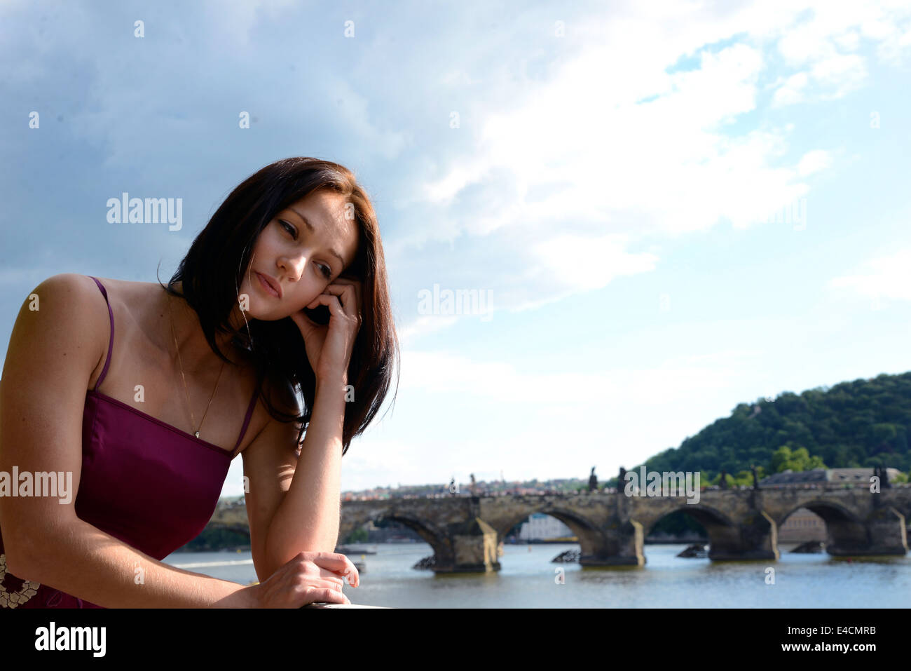 Attractive lady thinking with concern in front of a scenic bridge, river, mountain and sky Stock Photo