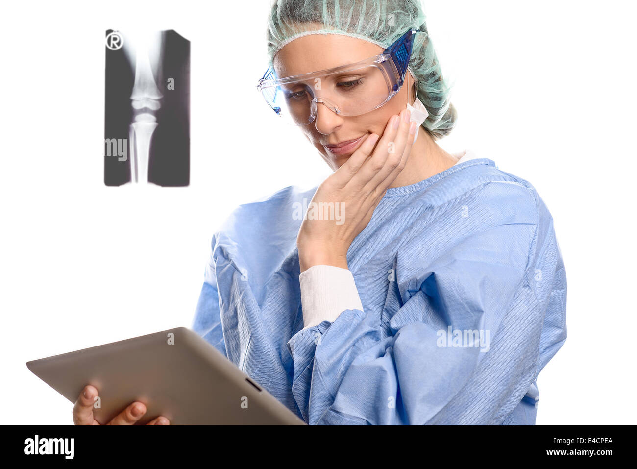 Attractive female surgeon or doctor in a mask, goggles and surgical gown standing consulting a tablet computer reading Stock Photo