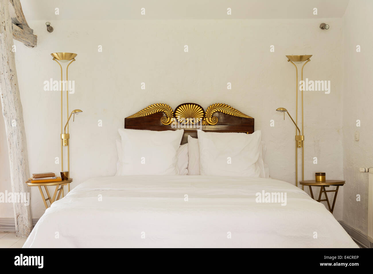 Gold standing lamps flanking white bed with gilt scalloped headboard Stock Photo