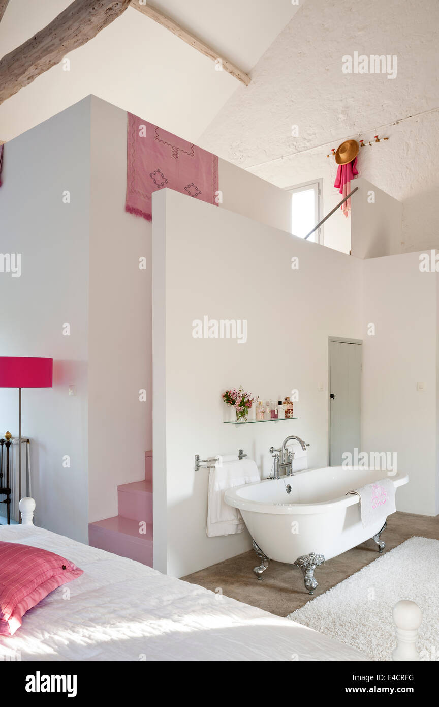 Freestanding bath in open plan bedroom with pink staircase Stock Photo