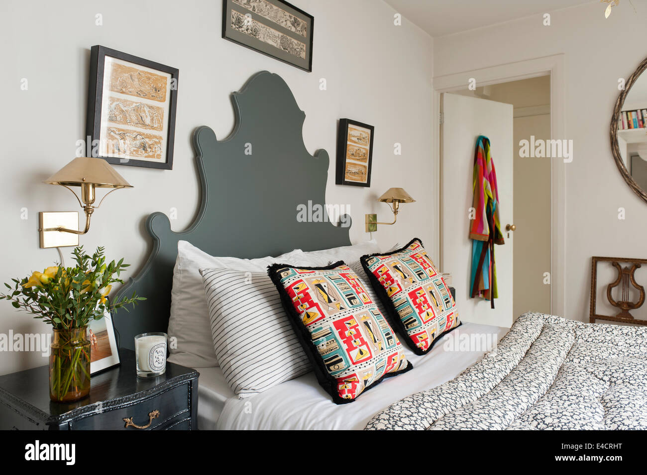 Vintage floral eiderdown on bed with Fabindia striped pillow cases and 50's cushions. The OKA headboard is painted in Downpipe b Stock Photo