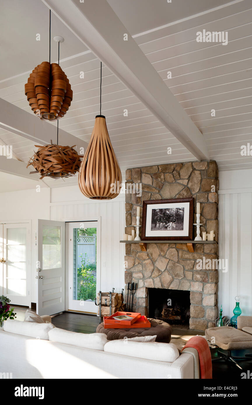 Open plan wood panelled white living space with rough stone fireplace and wood veneer lighting Stock Photo