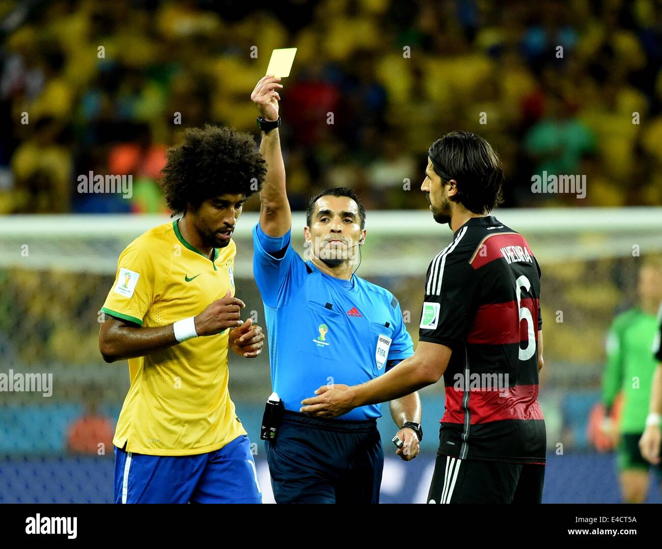 Belo Horizonte, Brazil. 8th July, 2014. Mexico's referee Marco Rodriguez (C) shows a yellow card to Brazil's Dante (L) during a semifinal match between Brazil and Germany of 2014 FIFA World Cup at the Estadio Mineirao Stadium in Belo Horizonte, Brazil, on July 8, 2014. Credit:  Liu Dawei/Xinhua/Alamy Live News Stock Photo