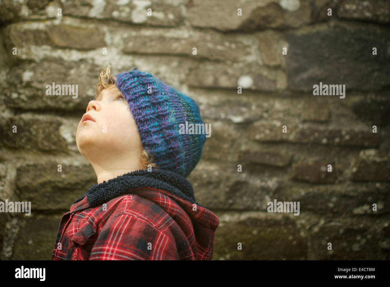 boy looks up against a stone wall Stock Photo