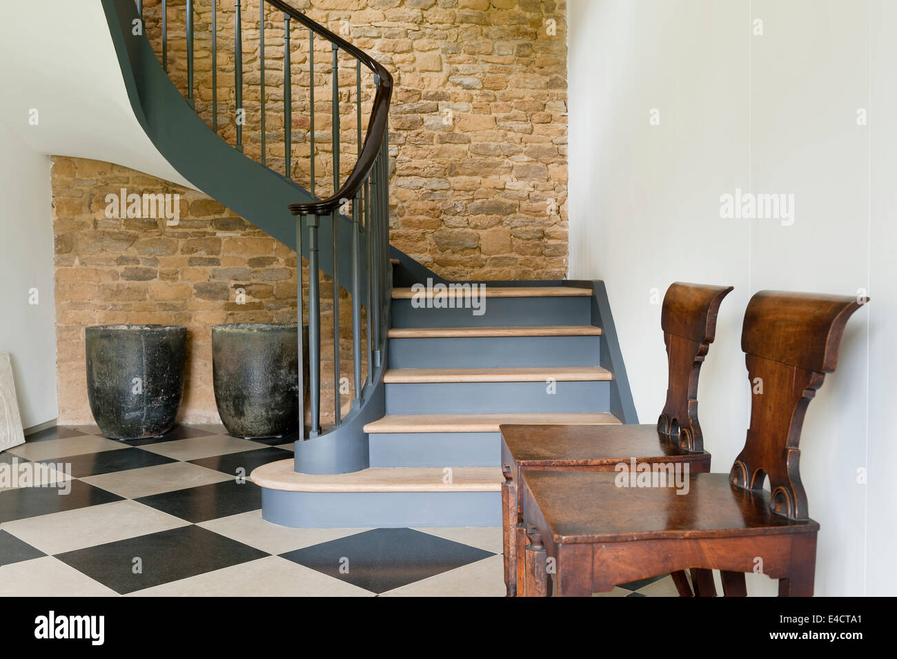 Pair of Willaim IV mahogany hall chairs in hallway with large checked flooring and swirling staircase Stock Photo