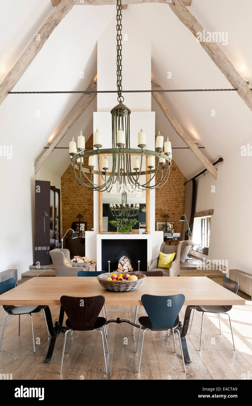 Verdigris chandelier hangs above an oak topped dining table in open plan living space with fireplace acting as partition. Stock Photo