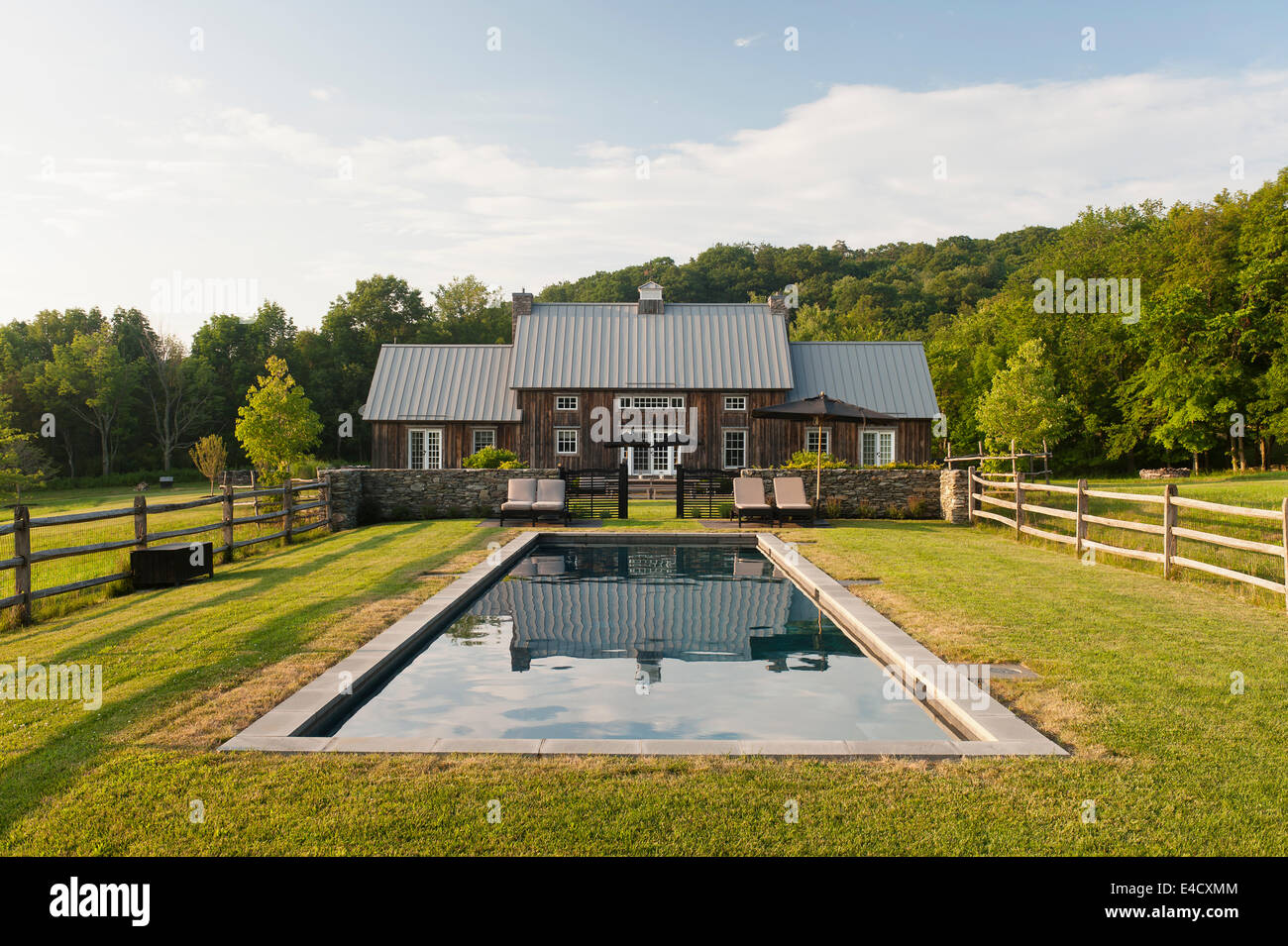 Outdoor pool with lawn surrounds in garden of timber-framed house on woodland edge Stock Photo