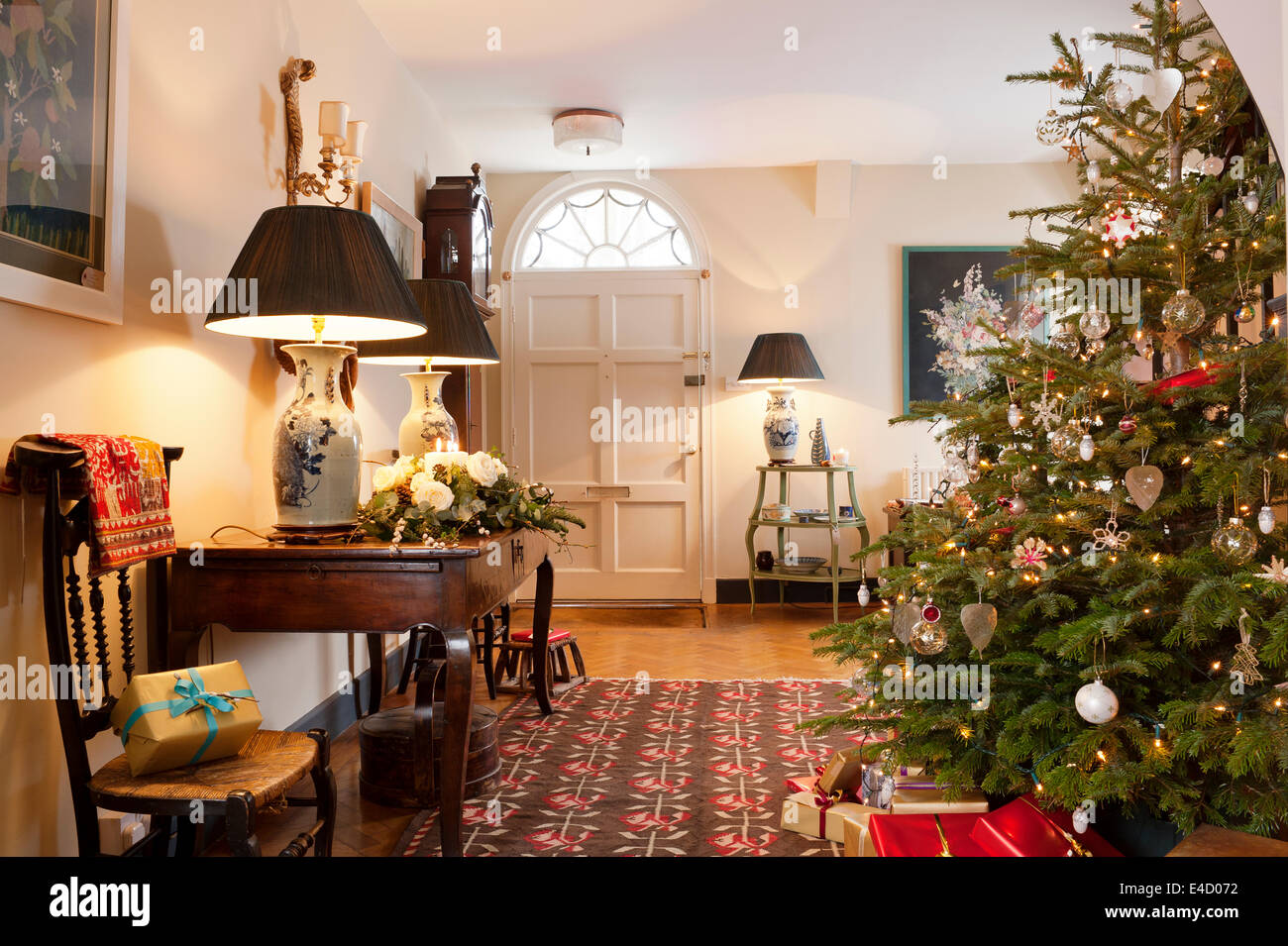 Christmas tree in entrance hall with early 20th century kilim. The hall table is French chestnut and the table lamps are antique Stock Photo