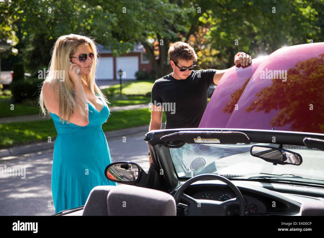A young women stands beside a broken down car calls a tow truck or auto ...