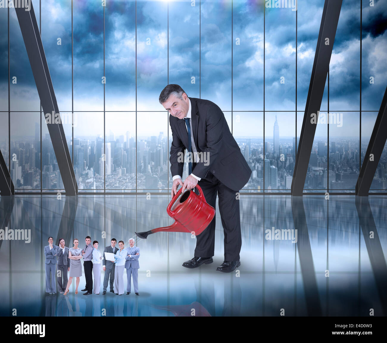 Composite image of mature businessman watering tiny business team Stock Photo