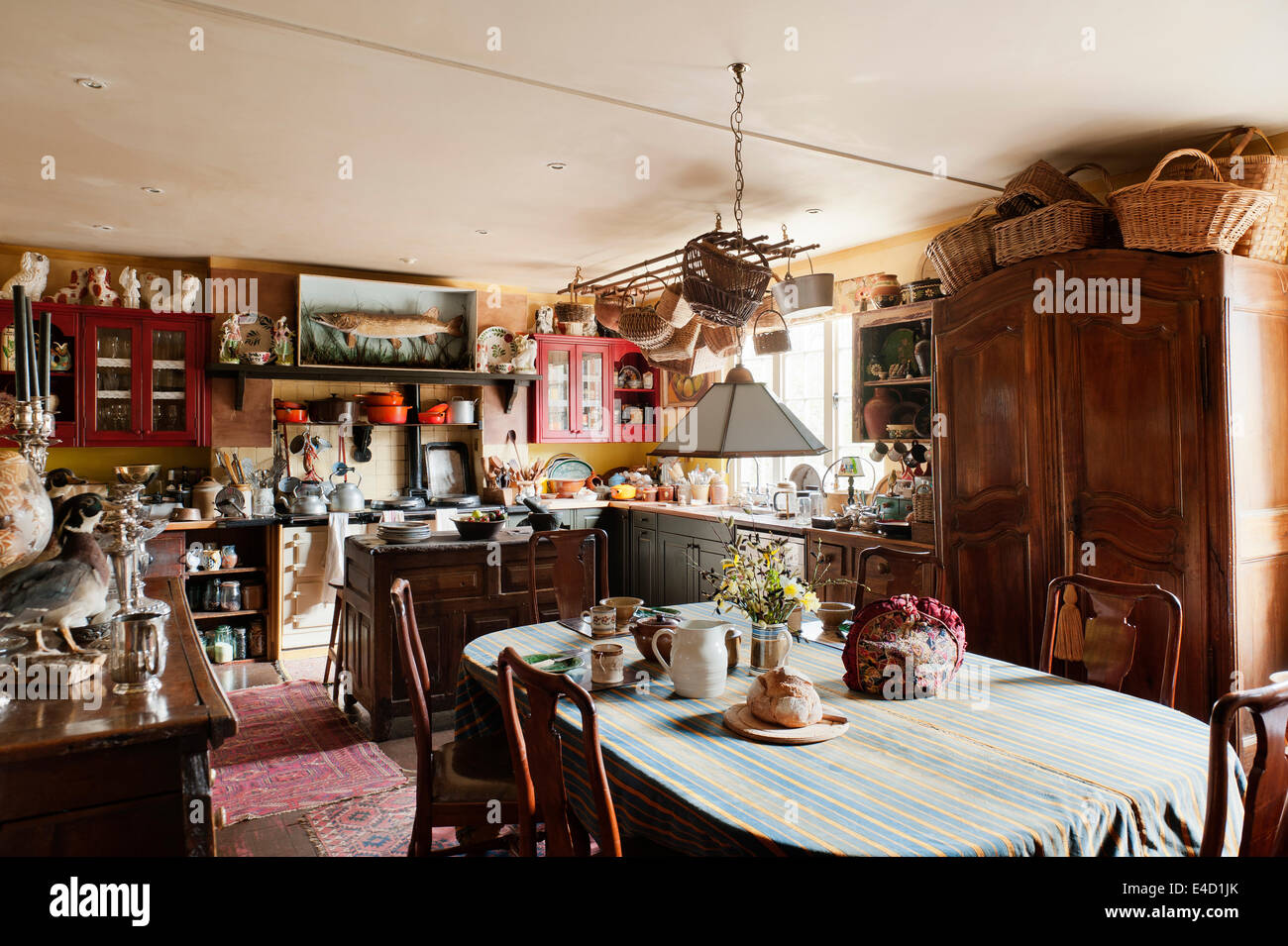 Charming country kitchen stuffed with antiques. Wicker baskets are piled on top of a large armoire and tea and bread are laid on Stock Photo