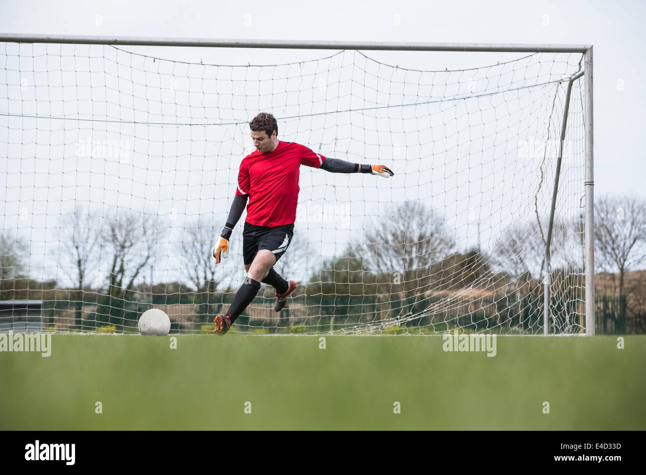 Goalkeeper Rushing Out Goalkeeper in red kicking ball away from goal Stock Photo - Alamy