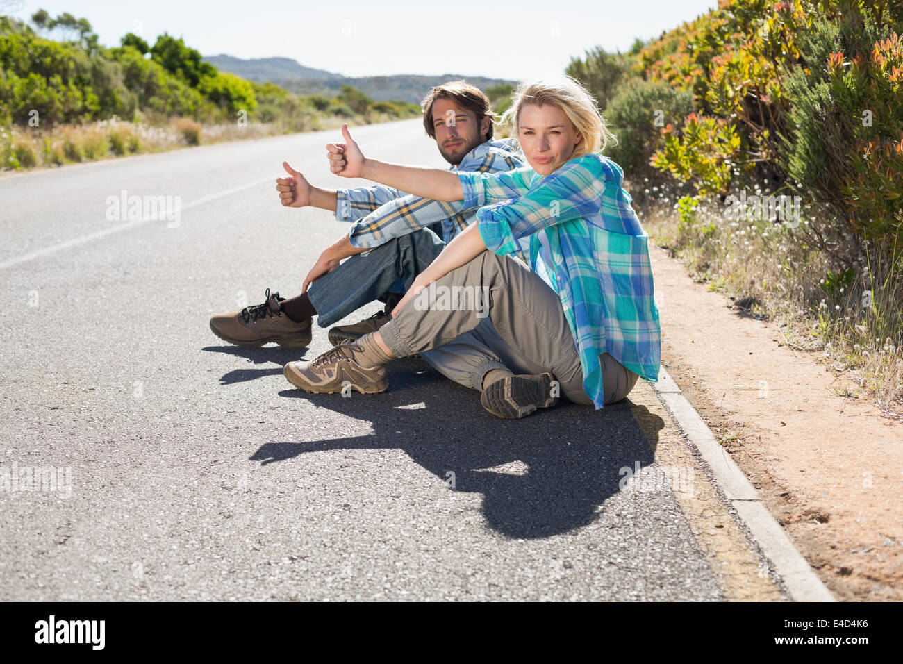 Attractive couple sitting on the road hitching a lift Stock Photo