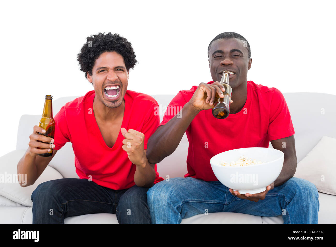 Football fans in red cheering on the sofa with beers and popcorn Stock Photo